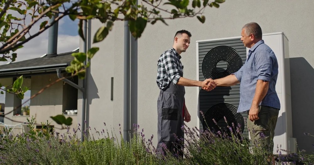 Homeowner shaking hands with an HVAC technician beside an outdoor unit