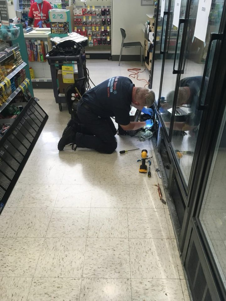 Cool Aid technician repairing a glass door cooler in a store